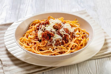Spaghetti al ragu alla Bolognese garniert mit geschreddertem Käse in weißer Schüssel auf weißem Holztisch, horizontale Ansicht von oben