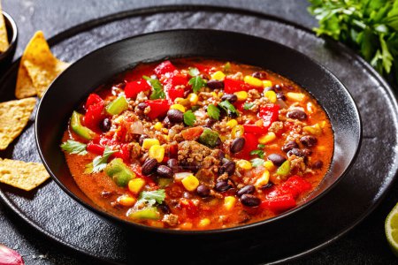taco soup of ground beef, tomatoes, chopped green chilis, onions, corn, red beans and taco seasoning in black bowl,  close-up,