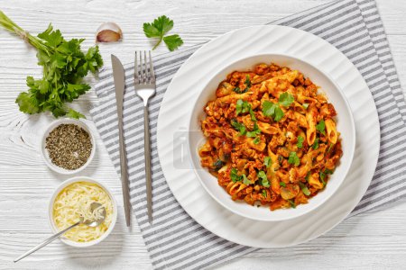 Ground Chicken Pasta Bake with onion, mushrooms, spinach, tomato sauce and mozzarella cheese in white bowl on white wood table, horizontal view from above, flat lay