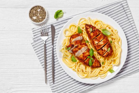 Chicken Scallopini of crusted chicken breast over lemon butter pasta on white plate on white wooden table, horizontal view from above, flat lay, free space