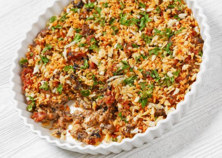delicious ground meat crumbles mushrooms casserole topped with panko breadcrumbs and parsley in baking dish on white wooden table, close-up