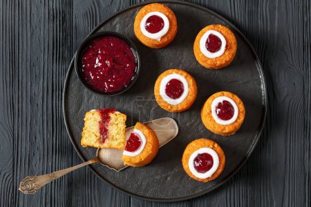 runebergin torttu, runeberg cakes, a finnish dessert flavored with almond, raspberry jam and rum on plate on black wooden table, horizontal view from above, flat lay, close-up