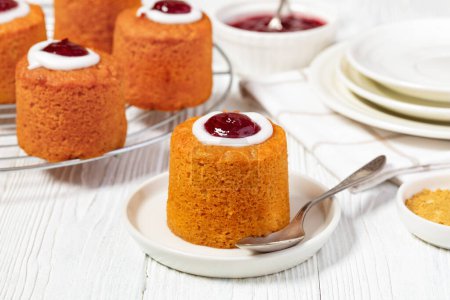 close-up of runebergin torttu, runeberg torte, finnish mini cake flavored with almond, raspberry jam and rum on plate with spoon on white wooden table, horizontal view from above