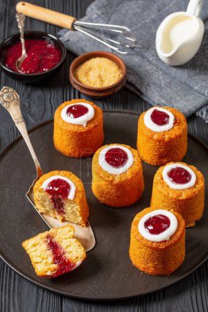 runebergin torttu, runeberg cakes, a finnish dessert flavored with almond, raspberry jam and rum on plate on black wooden table with ingredients, vertical view from above
