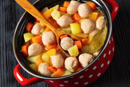 close-up of siskonmakkarakeitto, finnish sausage soup with rutabaga, potato, onion, carrot, parsnip in red pot, close-up, dutch angle view