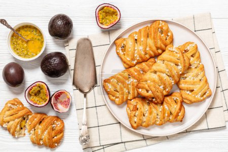 Passionsfrucht-Umsatz süße Kuchen auf Teller auf weißem Holztisch mit Kuchenschaufel, frische Passionsfrüchte, Horizontalblick von oben, flache Lage