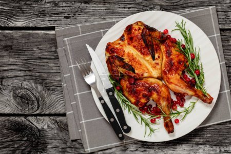 butterflied roast whole chicken on plate with rosemary and cranberry, on grey wooden rustic table with cutlery, horizontal view from above, flat lay, free space