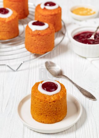 runebergin torttu, runeberg cake, a finnish mini cake flavored with almond, raspberry jam and rum on plate on white wooden table with ingredients, vertical view from above
