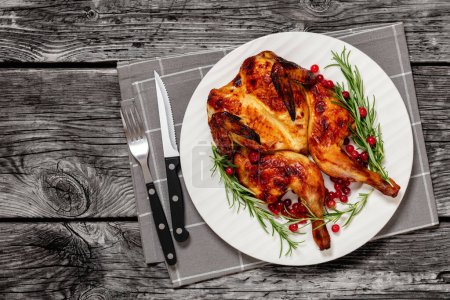 butterflied roast whole chicken on plate with rosemary and cranberry, on grey wooden rustic table with cutlery, horizontal view from above, flat lay, free space