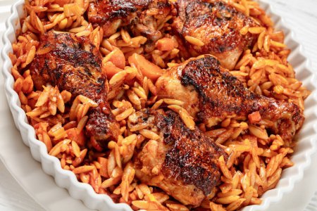 One pan baked greek chicken orzo stew in tomato based sauce, giouvetsi youvetsi in baking dish on white wooden table, close-up