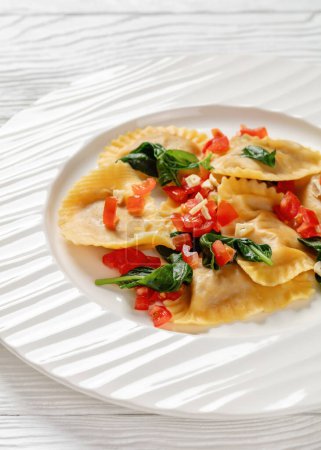 entresuelo de pasta italiana con tomates, ajo y albahaca sobre plato blanco con tenedor sobre mesa de madera blanca, vista vertical desde arriba, primer plano