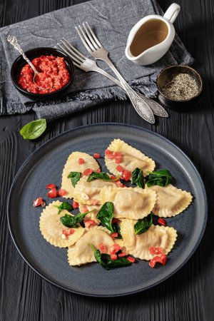 crescent-shaped pasta mezzelune with tomatoes, garlic and basil on grey plate on black wooden table, vertical view from above