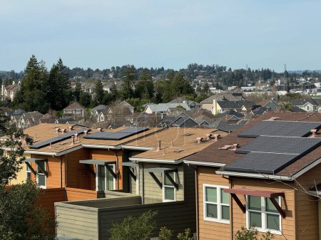 Dense suburban landscape showing rows of houses with varying roof designs and solar panels, nestled among trees