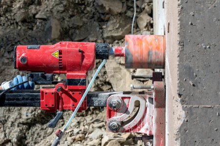 Photo for Worker is drilling to concrete wall with core drill machine. Core drills used in metal are called annular cutters. Core drills used for concrete and hard rock generally use industrial diamond grit. - Royalty Free Image