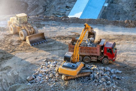 Foto de Yellow color excavator is loading some rocks to red color earth dump truck in the construction site. - Imagen libre de derechos