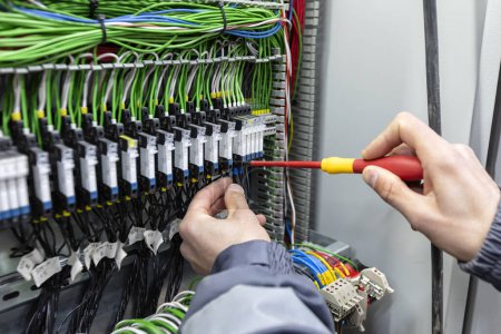 Foto de El electricista está conectando cables del panel de control eléctrico con un destornillador. - Imagen libre de derechos