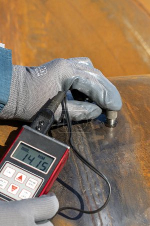 Photo for Inspector is measuring thickness of the pipe material from near to weld with a portable ultrasonic wall thickness measurement gauge. It is a method of performing non destructive measurement (gauging). - Royalty Free Image