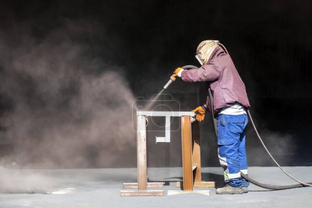 Foto de Sandblaster is sandblasting to steel material. Sand blasting is also known as abrasive blasting, which is a generic term for the process of smoothing, shaping and cleaning a hard surface by forcing. - Imagen libre de derechos
