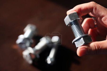 Photo for View of the bolts and nuts (fasteners). A bolt is a form of threaded fastener with an external male thread. Bolts are very closely related to screws. Bolts are often used to make a bolted joint. Metal bolts and nuts on a dark wooden background. - Royalty Free Image