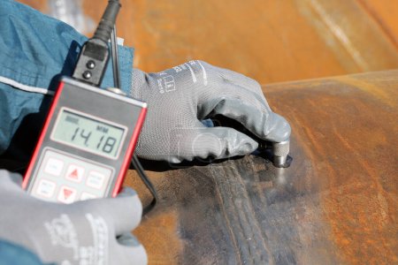 Photo for Inspector is measuring thickness of the pipe material from near to weld with a portable ultrasonic wall thickness measurement gauge. It is a method of performing non destructive measurement (gauging). - Royalty Free Image