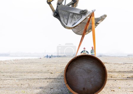 Photo for Excavators are lifting a large steel pipe pile and occupational safety specialists control the operation. The specialists analyze many types of work environments and work procedures. - Royalty Free Image