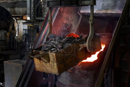 Photo for A large metal oven with a fire in the background. The melting metal is pouring to big melting pot in the industrial foundry plant. Metals are cast into shapes by melting them into a liquid, pouring the metal into a mold. - Royalty Free Image