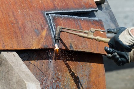 Foto de The worker is cutting to metal plate with manual flame cutting process. Oxy-fuel welding, oxyacetylene welding, oxy welding, or gas welding and oxy-fuel cutting are processes that use fuel gases. - Imagen libre de derechos