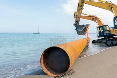 Photo for Excavators are carrying pile pipe to sea. Pipe piles are either a welded or seamless steel pipe which may be driven either open-ended or closed-ended. It is easy to understand type of piling. - Royalty Free Image