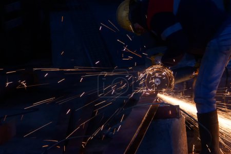 Foto de Trabajador industrial de corte de metal con amoladora angular en una fábrica. El trabajador está cortando un material de acero con una rectificadora en el sitio de construcción. - Imagen libre de derechos