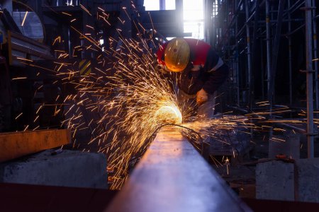 Téléchargez les photos : Travailleur industriel de coupe de métal avec meuleuse d'angle dans une usine. Le travailleur coupe un matériau en acier avec une rectifieuse sur le chantier. - en image libre de droit