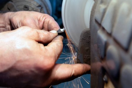 Téléchargez les photos : Travailleur utilisant un broyeur pour couper le métal. Broyage pour percer la mèche avec une rectifieuse à banc. Une meuleuse de banc est un type de meuleuse de plan de travail utilisé pour entraîner des roues abrasives. - en image libre de droit