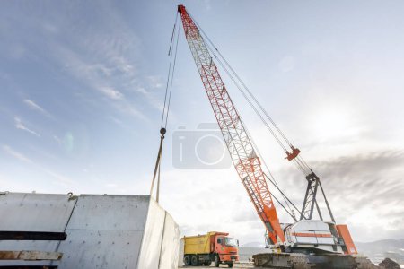 Photo for The big crawler crane and other construction machineries are working to build pier of the harbor. A crawler crane has its boom mounted on an undercarriage fitted with a set of crawler tracks. - Royalty Free Image