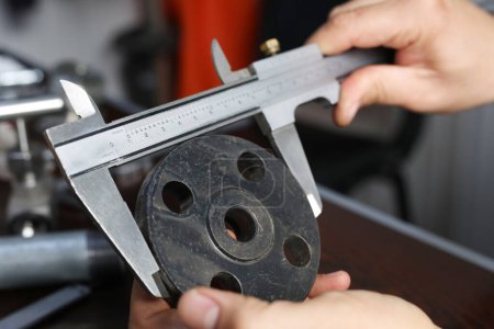 The worker is measuring to outer diameter of flange with vernier caliper gauge. Vernier calipers are widely used in scientific laboratories and in manufacturing for quality control measurements.