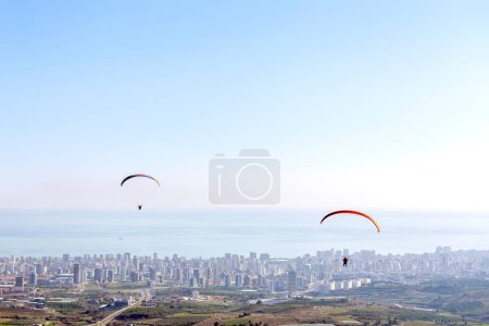 Foto de Paisaje de la ciudad, mar Mediterráneo y parapente sobre la ciudad. Tres parapentes vuelan juntos en Mersin, Turquía. - Imagen libre de derechos