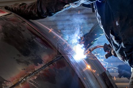 Téléchargez les photos : The welder is welding to steel material with gas metal arc welding proces. It sometimes referred to by its subtypes metal inert gas (MIG) welding or metal active gas (MAG) welding. - en image libre de droit