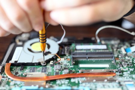 Photo for Expert is repairing to inner of laptop with screwdriver. The design restrictions on power, size, and cooling of laptops limit the maximum performance of laptop parts compared. - Royalty Free Image