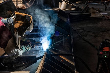The welder is welding a structural steel with gas metal arc welding ( GMAW ) in the workshop. Welder welding metal with sparks in workshop
