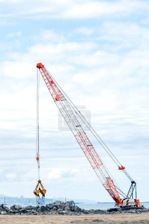 Photo for The big crawler crane and other construction machineries are working to build pier of the harbor. A crawler crane has its boom mounted on an undercarriage fitted with a set of crawler tracks. - Royalty Free Image
