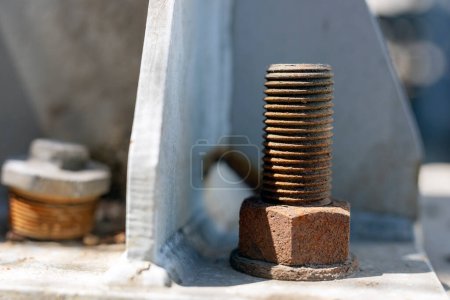 Photo for A rusty steel anchor bolt on the flange of the structure steel. Anchor bolts are used to connect structural and non-structural elements to concrete. Old rusty metal screws on the background of the house. - Royalty Free Image