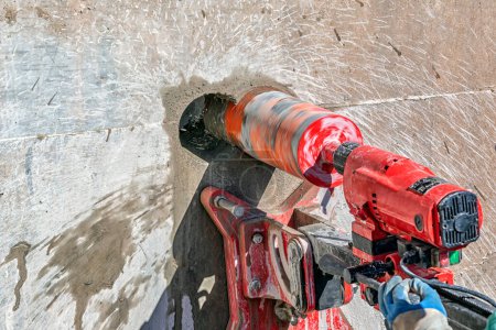 Foto de Worker is drilling to concrete wall with core drill machine. Core drills used in metal are called annular cutters. Core drills used for concrete and hard rock generally use industrial diamond grit. - Imagen libre de derechos