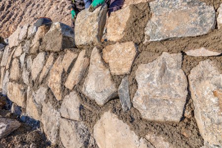 Téléchargez les photos : Les ouvriers construisent un mur de pierre. Les murs de pierre sont généralement faits de matériaux locaux allant du calcaire et du silex au granit et au grès.. - en image libre de droit
