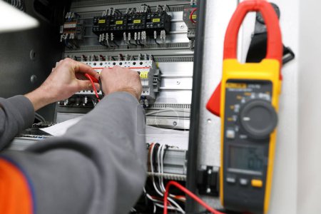 Photo for Electrician is measuring voltage of switchgear with clamp meter. it is composed of electrical disconnect switches, fuses or circuit breakers used to control, protect and isolate electrical equipment. - Royalty Free Image