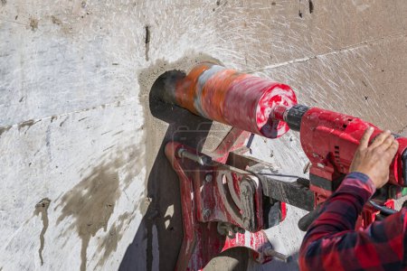 Téléchargez les photos : Worker is drilling to concrete wall with core drill machine. Core drills used in metal are called annular cutters. Core drills used for concrete and hard rock generally use industrial diamond grit. - en image libre de droit