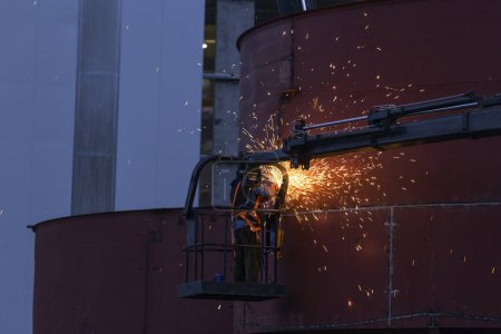 Foto de El soldador está soldando y moliendo en los tanques de espesante en el sitio de construcción (Serie -2). - Imagen libre de derechos