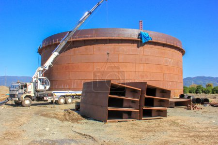 Photo for View of the manufacturing and assembly of the big crude oil storage tank with floating roof. The crane is lifting pontoons of the storage tank. - Royalty Free Image