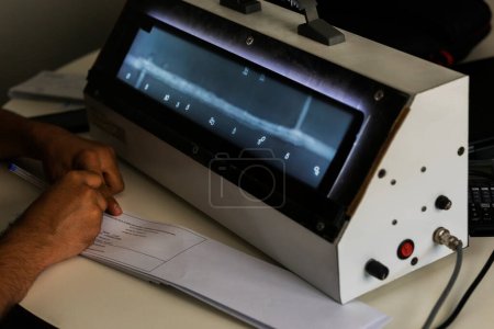 Foto de El operador de radiografía nivel 2 radiografías de evaluación de las soldaduras con el espectador y está escribiendo algunos informes. Ndt. - Imagen libre de derechos