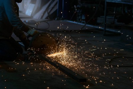 Foto de El trabajador del metal que corta un material de acero con la máquina de sierra circular y chispas en el taller. - Imagen libre de derechos