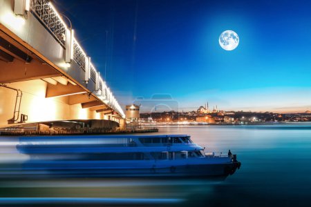 Beautiful night landscape of Galata bridge, full moon, lights, passenger boat and bosphorus of golden horn, Istanbul in Turkey.