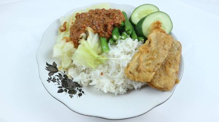 Photo for Pecel is a traditional Indonesian food made from a mixture of boiled vegetables such as cabbage and green beans with peanut sauce as a seasoning. Served with fried tempeh and crackers. Isolated white - Royalty Free Image