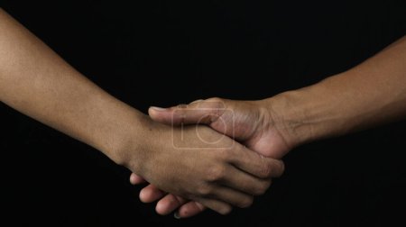 Nahaufnahme zweier Männer beim Händeschütteln als Übereinkunft auf schwarzem Hintergrund.